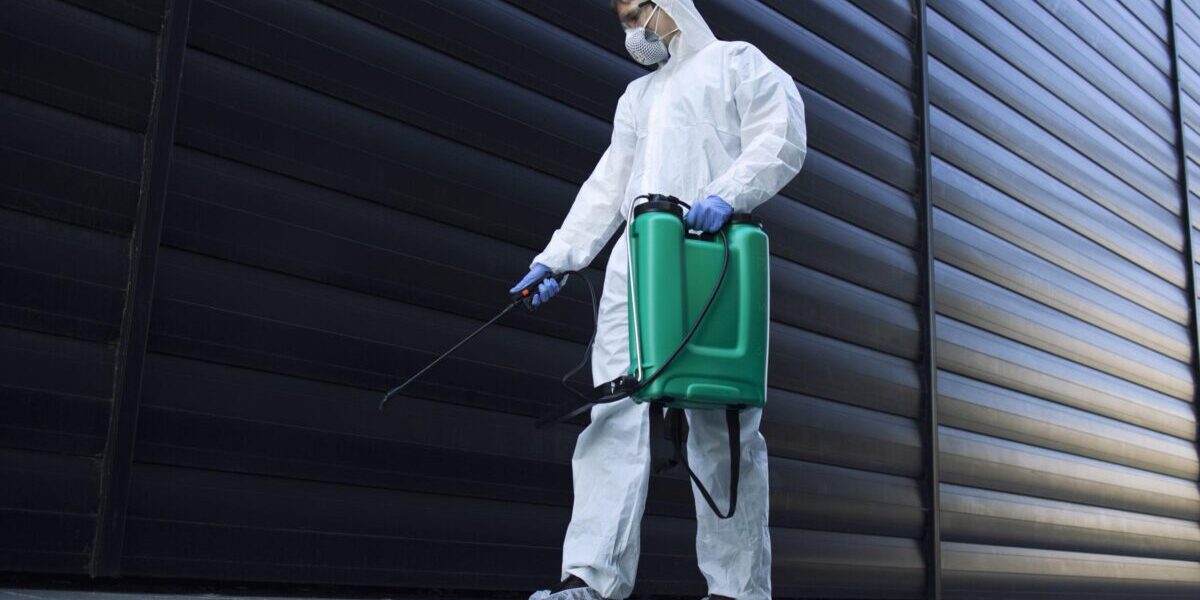 Person in white chemical protection suit doing disinfection of public areas to stop spreading highly contagious corona virus.