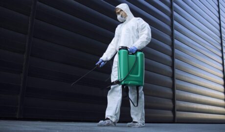 Person in white chemical protection suit doing disinfection of public areas to stop spreading highly contagious corona virus.